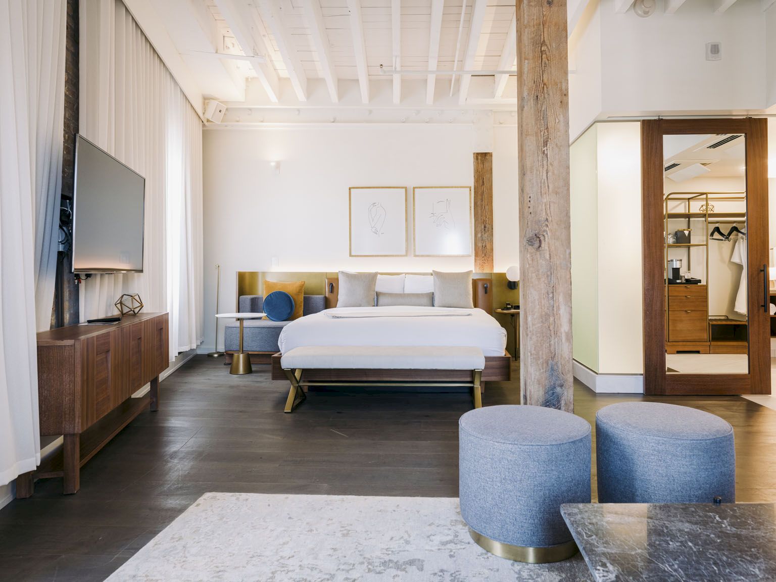A bright, modern hotel room with a king bed, seating area, wood accents, and a doorway to a closet or ensuite, airy and stylish.