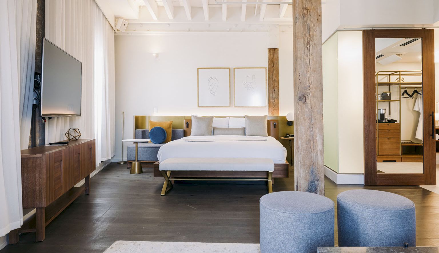 A bright, modern hotel room with a king bed, seating area, wood accents, and a doorway to a closet or ensuite, airy and stylish.