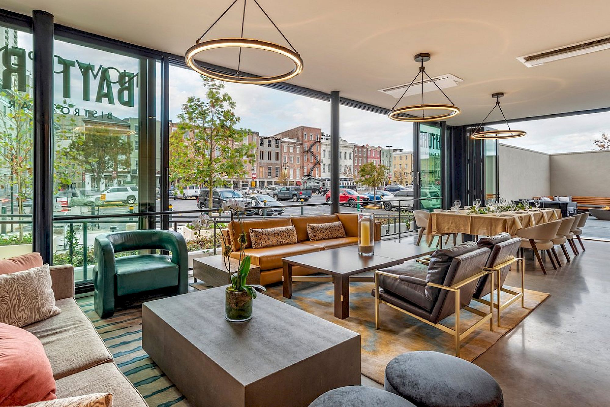 A modern, airy lounge with large windows, mid-century sofas, coffee tables, green plants, and circular pendant lights by the windows, inviting and bright.