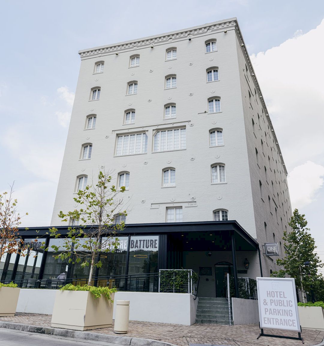 A modern white hotel building with windows, a glass entry, and a sign reading &ldquo;Hotel & Public Parking Entrance&rdquo;.