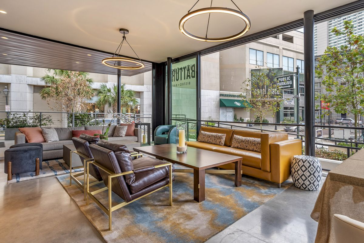 An outdoor lounge patio with leather and cushioned seating, modern ring lights, plants, and a city view with a Starbucks sign nearby.