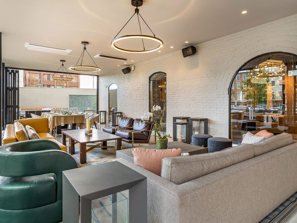 A modern lounge and dining area with white brick walls, arched windows, and pendant lights glowing overhead.