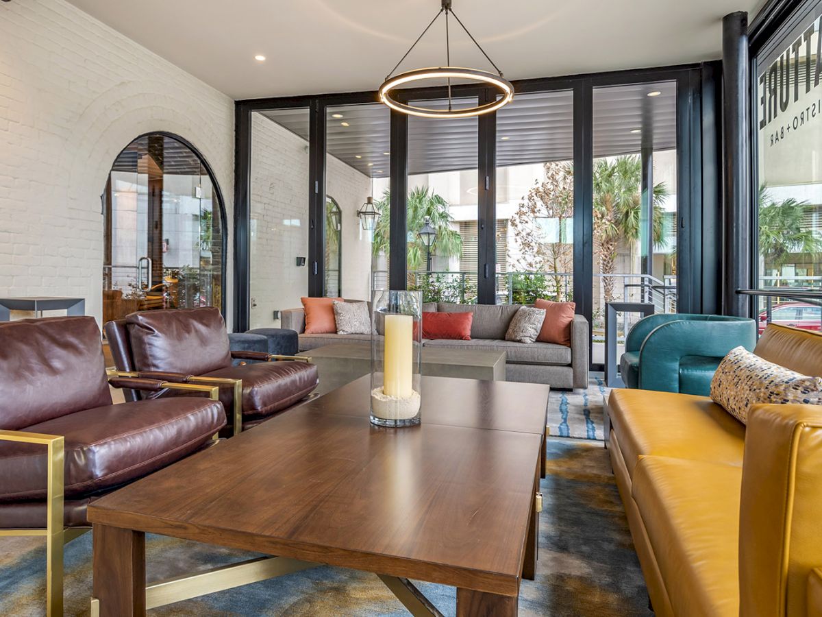 A modern lounge with leather sofas, colorful cushions, a wooden coffee table, and a glowing ring pendant light by large windows.