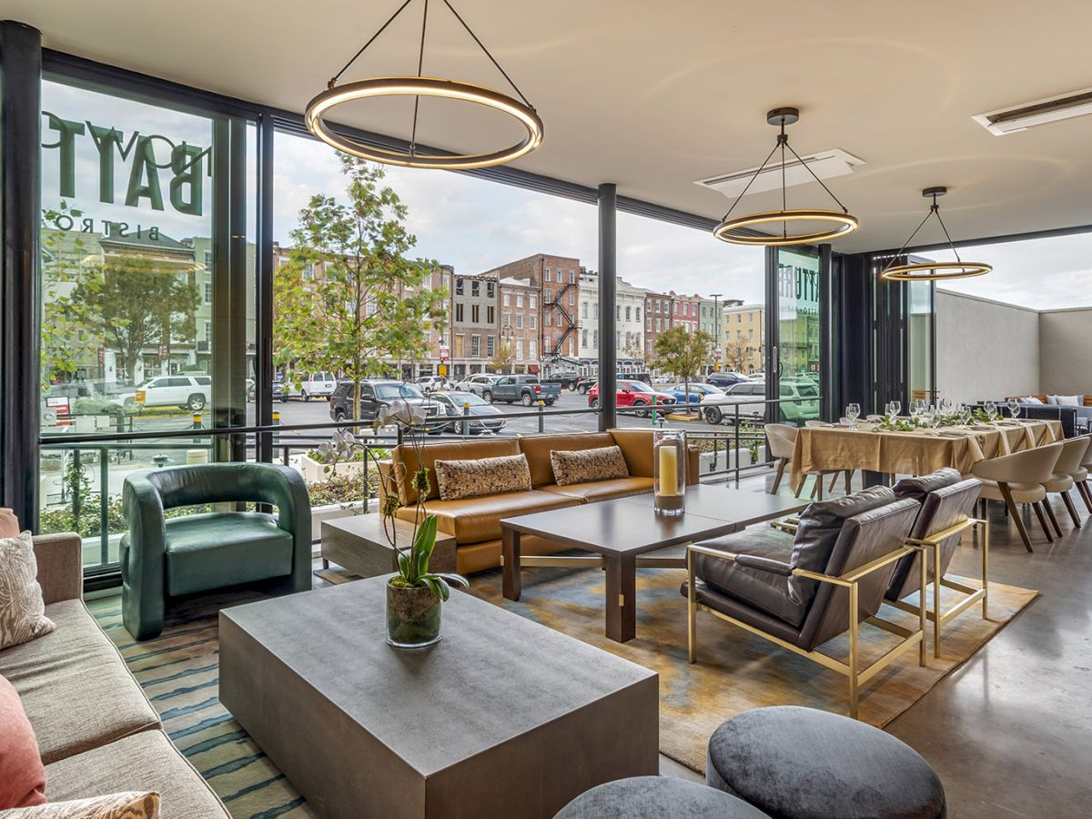 A modern lounge dining area with sofas and tables by big windows, warm hanging ring lights, and a street view outside.