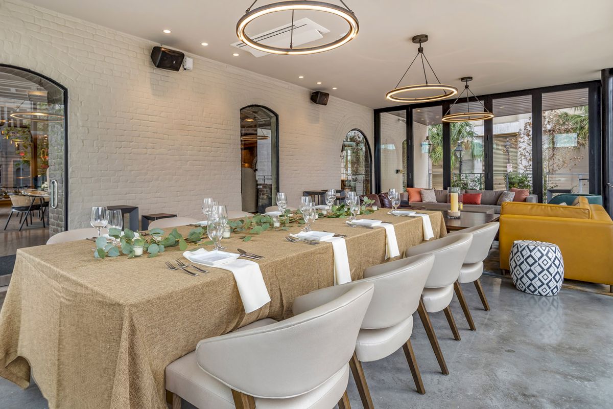 A modern dining room with set tables, white chairs, warm pendant lights, and large arched doorways opening to greenery, .