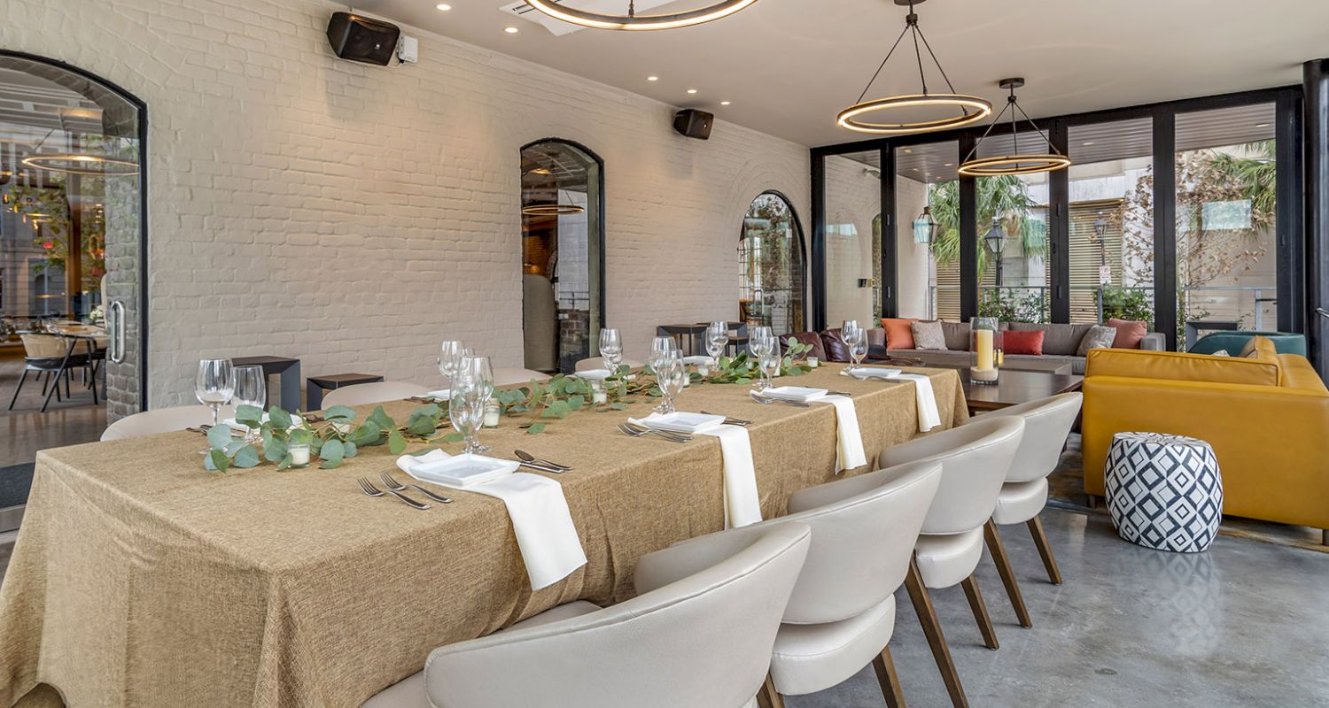 A dining room with a long table set for a meal, surrounded by white chairs and decorated with eucalyptus and candles.
