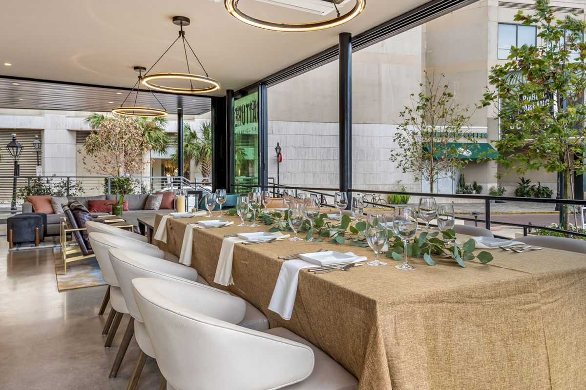 An upscale outdoor dining patio with neatly set tables, wine glasses, warm pendant lights, and potted greenery, on a modern terrace.