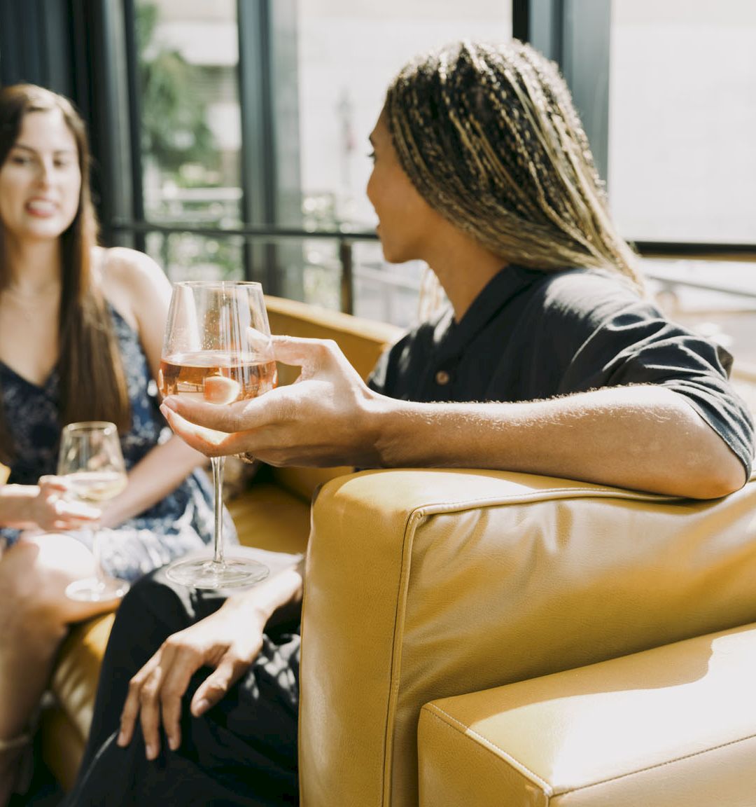 Two friends clink glasses of champagne at a cozy lounge, smiling as they toast together.