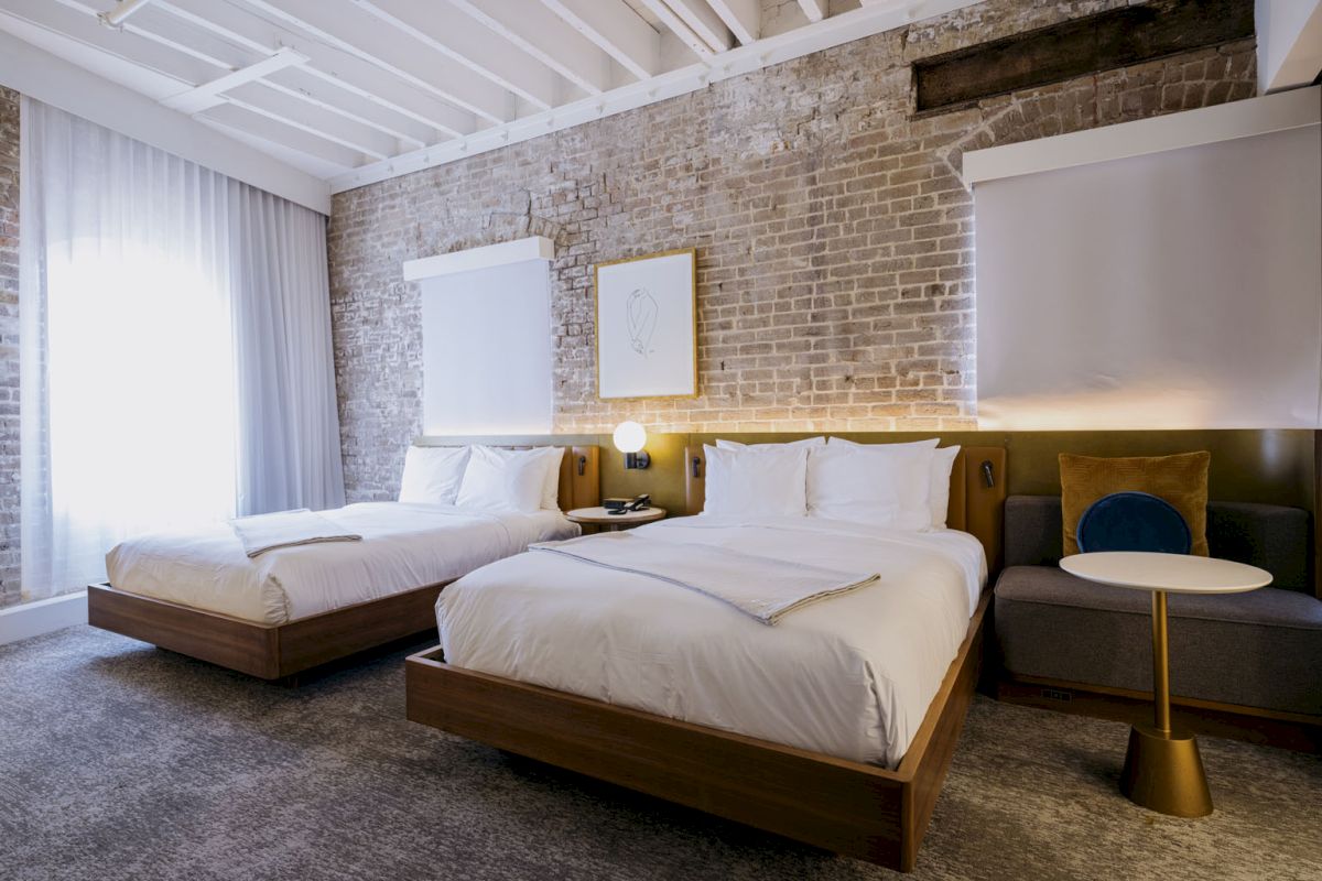 A modern hotel room with two neatly made twin beds, brick walls, and minimalist decor.