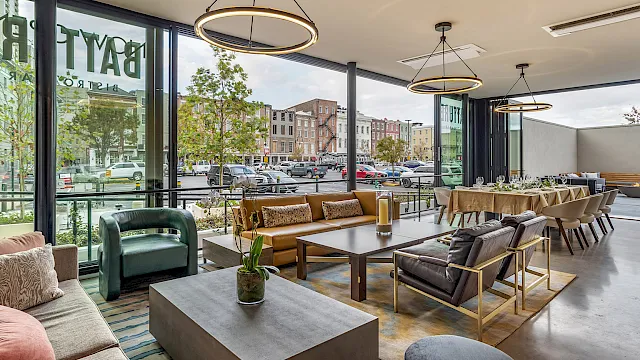 Modern lounge with sofas and dining tables, hanging ring lights, and large windows overlooking a busy street.