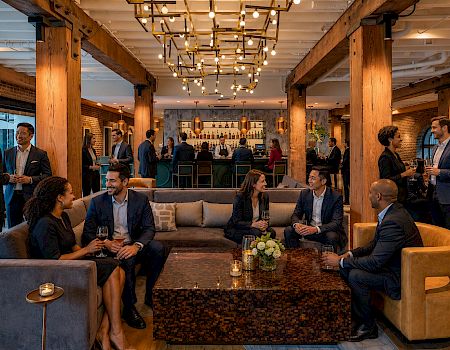 Friends in a modern bar lounge chat and toast with drinks under warm hanging lights.