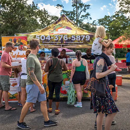 A crowd browses a Fresh Fruit Sensations food truck stand at an outdoor event under a sunny tent.