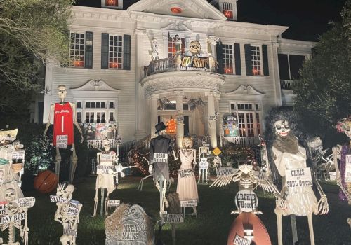A spooky, Halloween-style haunted house at night, filled with skeleton figures, tombstones, and creepy props on the lawn.