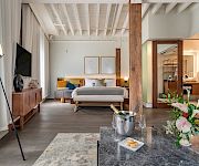 A modern bedroom with a large bed, TV and artwork, plus a coffee table, flowers, and warm lighting.
