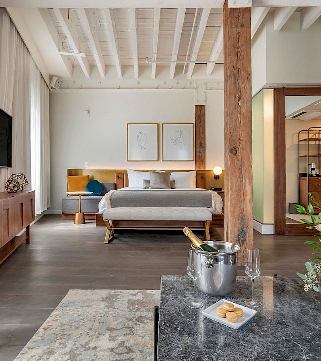 A modern bedroom with a large bed, TV and artwork, plus a coffee table, flowers, and warm lighting.