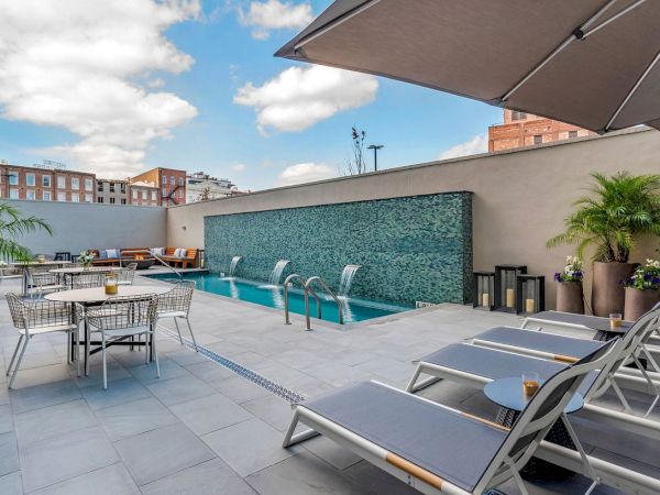 Sunny rooftop patio with a turquoise-tiled pool, lounge chairs, and outdoor dining under a beige awning.
