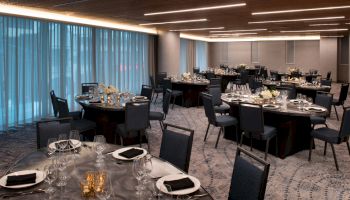 A banquet hall set for an event, with round tables covered in dark cloth, neatly arranged chairs, elegant table settings, and decorative centerpieces.