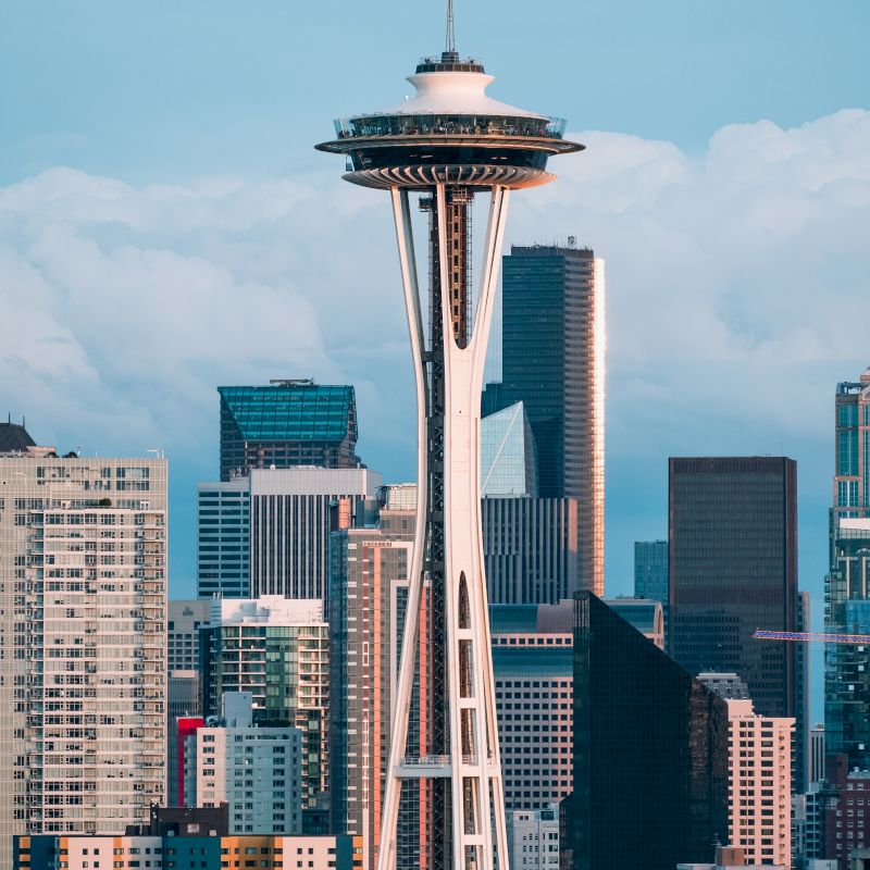 The image shows the Space Needle, an iconic observation tower in Seattle, with the city's skyscrapers in the background under a partly cloudy sky.