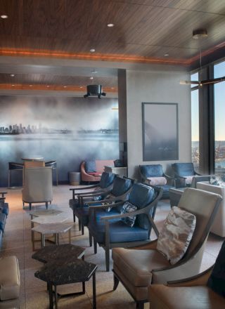 A spacious lounge with comfortable seating, large windows offering a scenic waterfront view, and a mural on the wall depicting a cityscape.