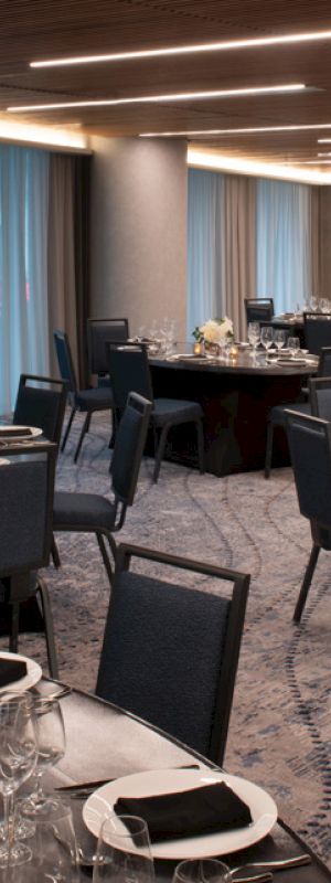 A banquet hall with round tables set with elegant dinnerware and floral centerpieces, and modern lighting overhead.